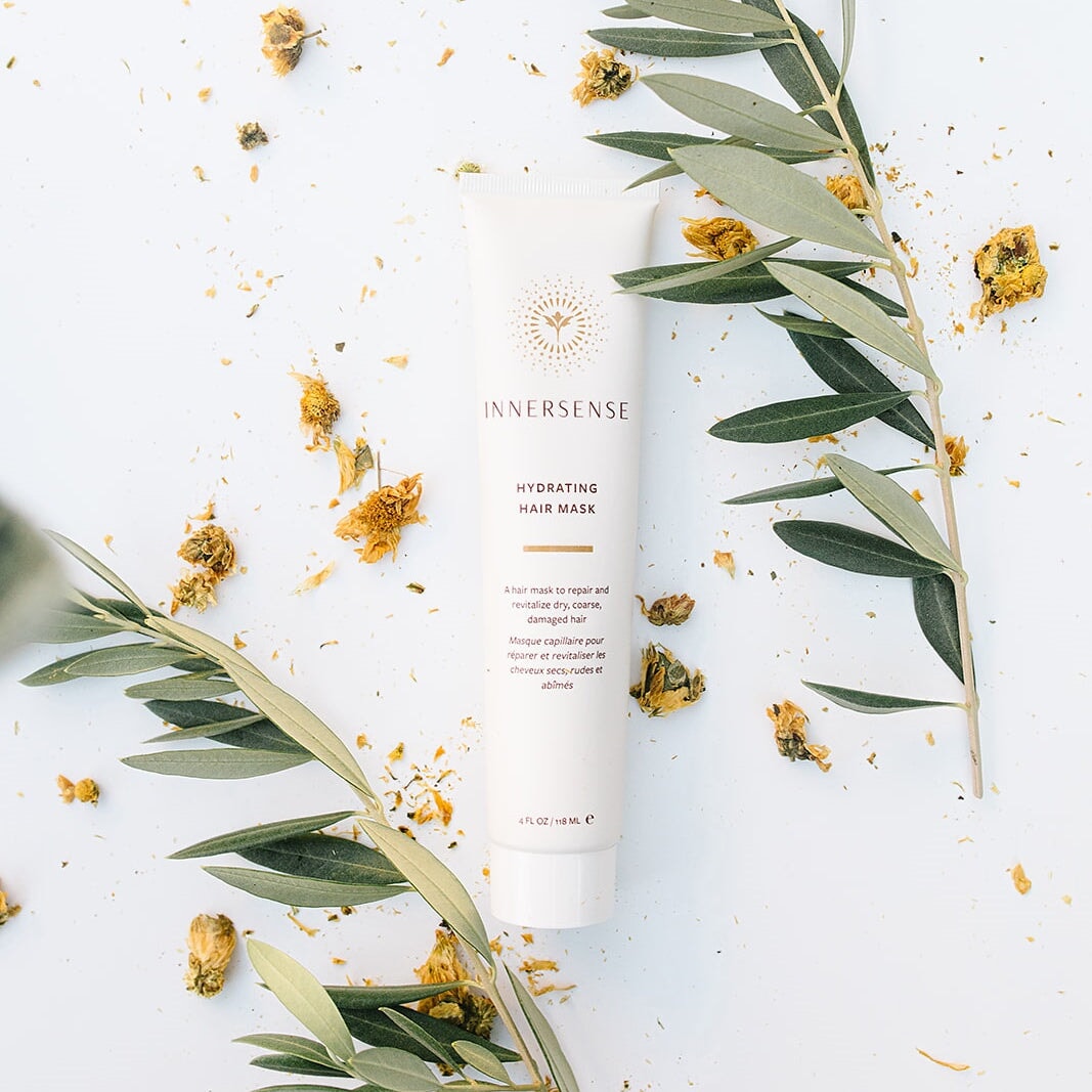 Innersense Hydrating Hair Mask Tube liegt zwischen Zweigen und getrockneten Blütenblättern.