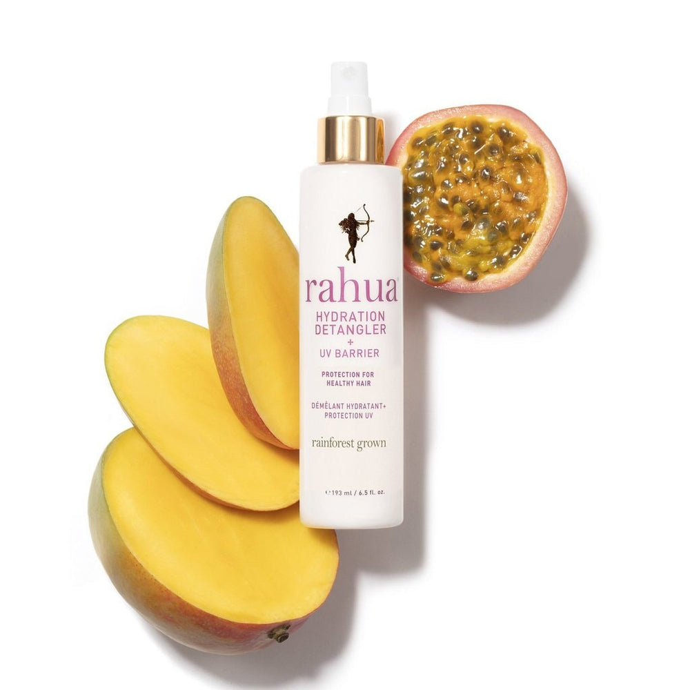 Rahua Hydration Detangler Flasche vor weißem Hintergrund dekoriert mit aufgeschnittener Mango und Maracuja.