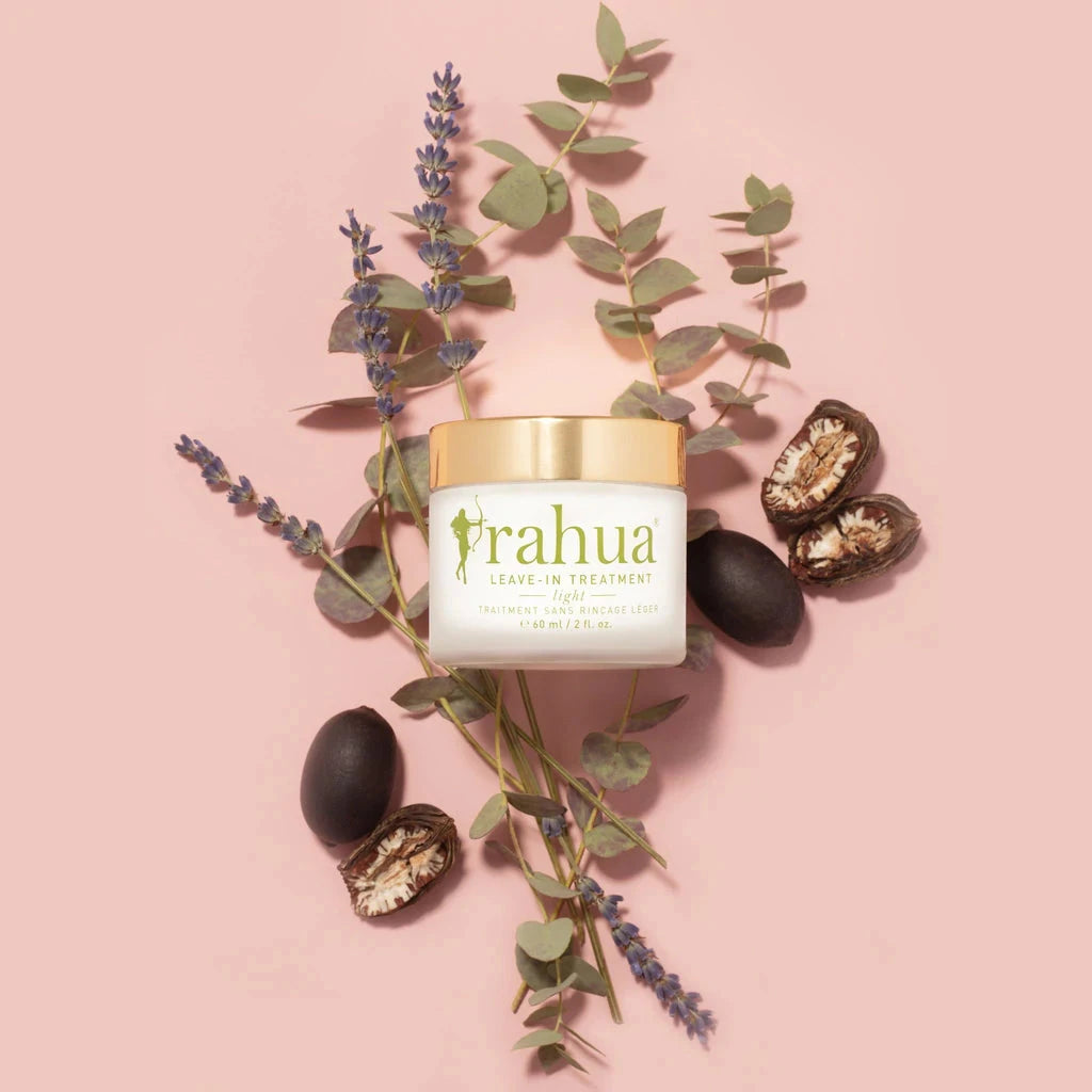 Rahua Leave-In Treatment Glas mit Schraubdeckel vor rosafarbenem Hintergrund, dekoriert mit Lavendel, Eukalyptus und Rahaunüssen.. North Glow