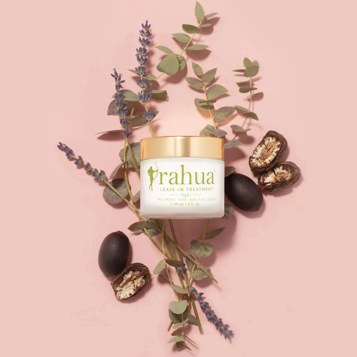 Rahua Leave-In Treatment Glas mit Schraubdeckel vor rosafarbenem Hintergrund, dekoriert mit Lavendel, Eukalyptus und Rahaunüssen..