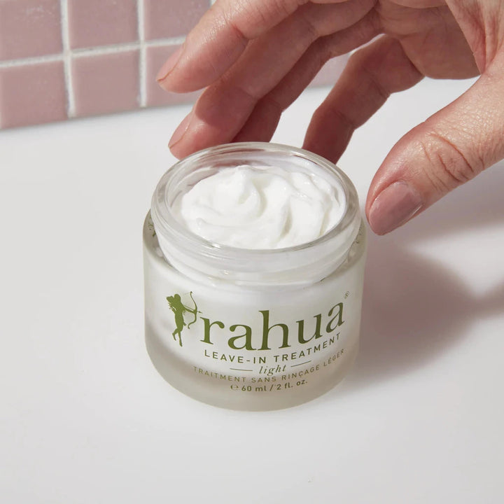 Hand greift nach Rahua Leave-In Treatment Glas, offen vor weißem Hintergrund.