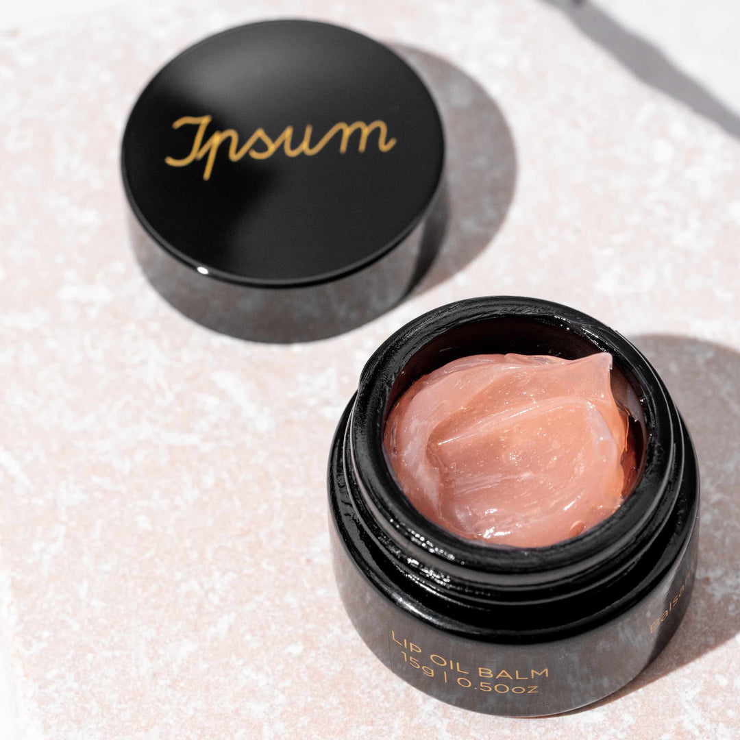 Schwarzer Ipsum Lip Oil Balm Tiegel steht offen, daneben liegt der Deckel, Balm im zarten Rosa und geschmeidiger Textur gut zu erkennen. North Glow