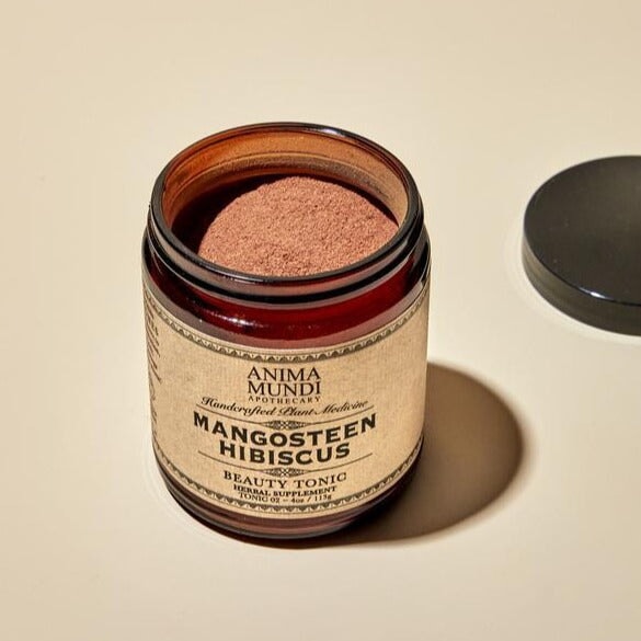 Offenes Schraubglas Mangosteen Hibiscus von Anima Mundi steht auf hellem Untergrund neben dem schwarzem Deckel.