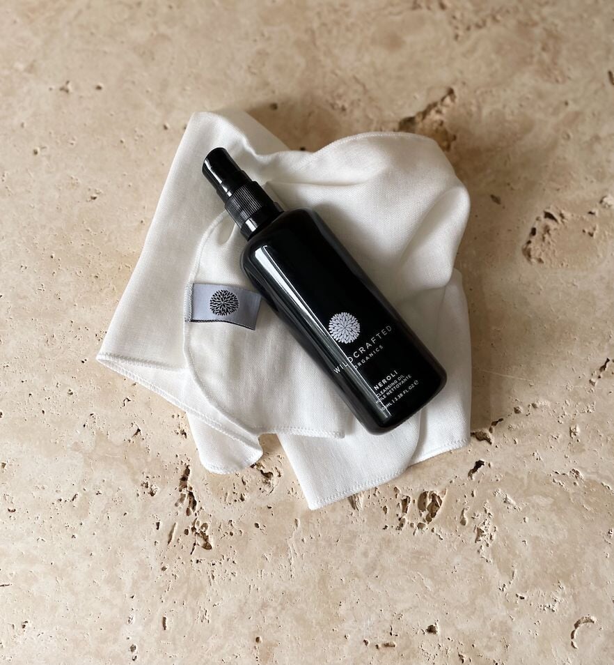Schwarze Pumpflasche von Wildcrafted Organics Neroli Cleanser liegt auf einem weißen Musselintuch.