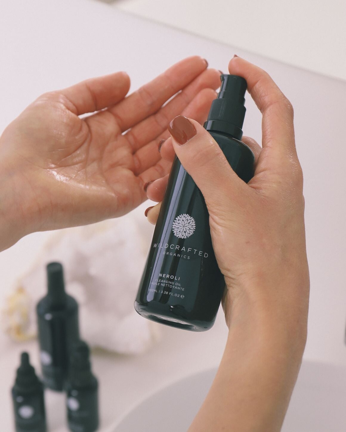 Hand hält Schwarze Pumpflasche von Wildcrafted Organics Neroli Cleanser und pumpt Inhalt in die andere Hand.
