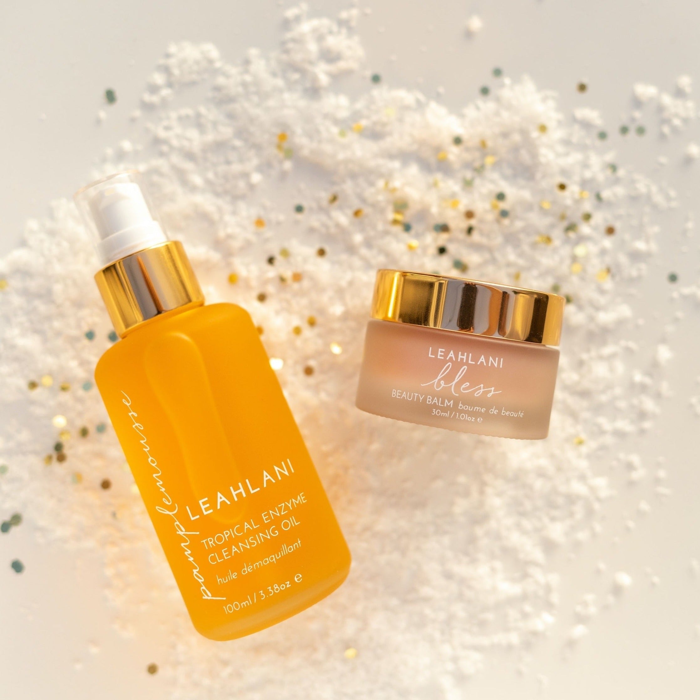 Leahlani Pamplemousse Cleansing Oil Flasche  und Bless Balm auf weißem sandigen Hintergrund