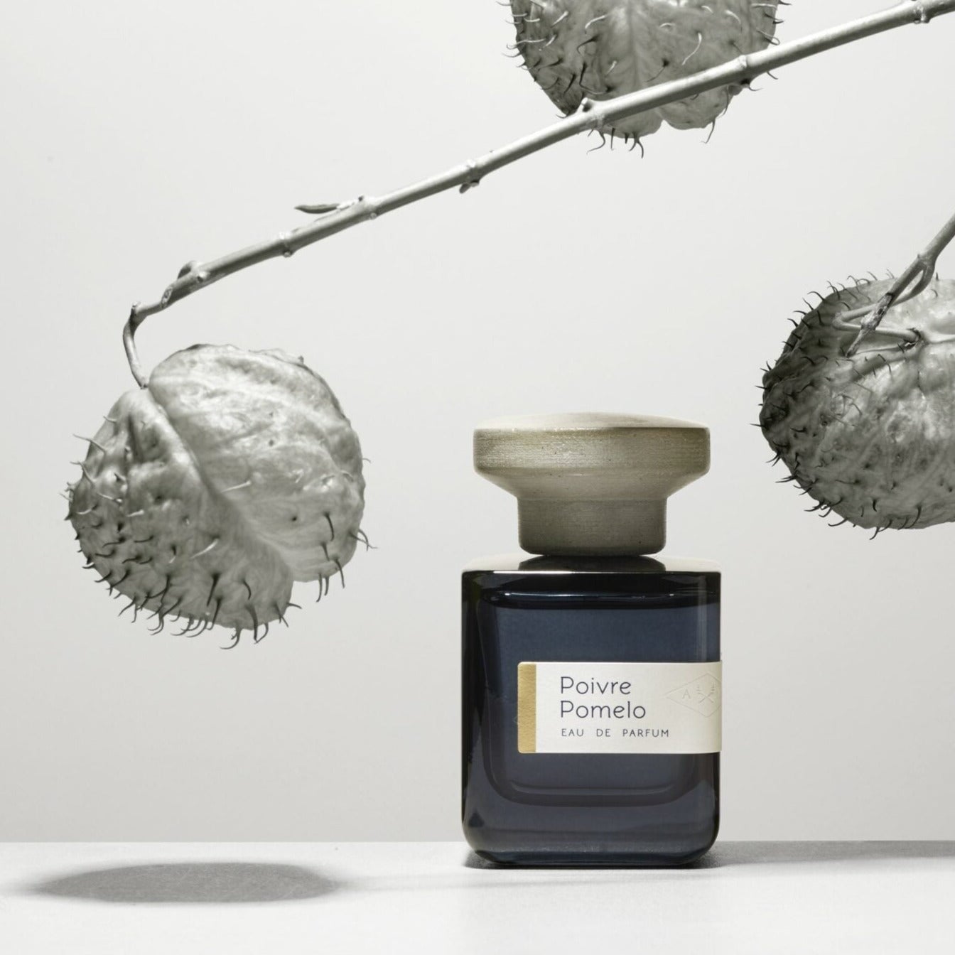 AtelDunkelblaue Glasflasche mit grauem Deckel "Poivre Pomelo" von Atelier Materi  stehend.