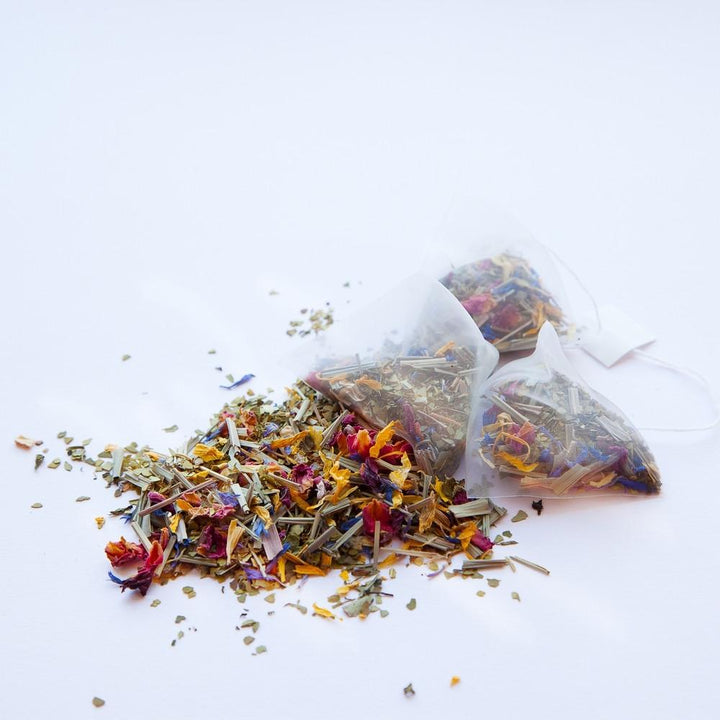 Lola's Apothecary Rainbows & Whirlwinds Teebeutel mit verstreutem, loosem Teem auf weißem Untergrund.