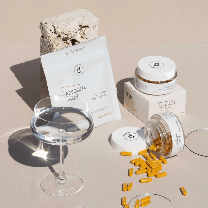 Depuravita Absolute Shine Refill Sachet und Tiegel mit Wasserglas vor beigen Hintergrund