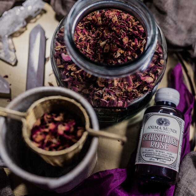 Anima Mundi Glasflasche Schisandra Rose  liegt neben einem Glas gefüllt mit getrockneten Rosenbättern.