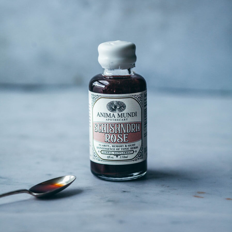 Anima Mundi Glasflasche Schisandra Rose  steht neben einem Löffel vor grauem Hintergrund.