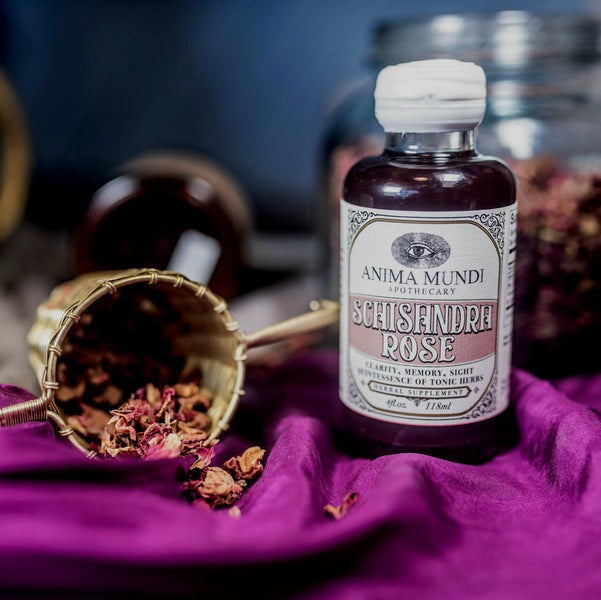 Anima Mundi Glasflasche Schisandra Rose  steht auf beerenfarbener Tischdecke, dekoriert mit getrockneten Rosenblättern.