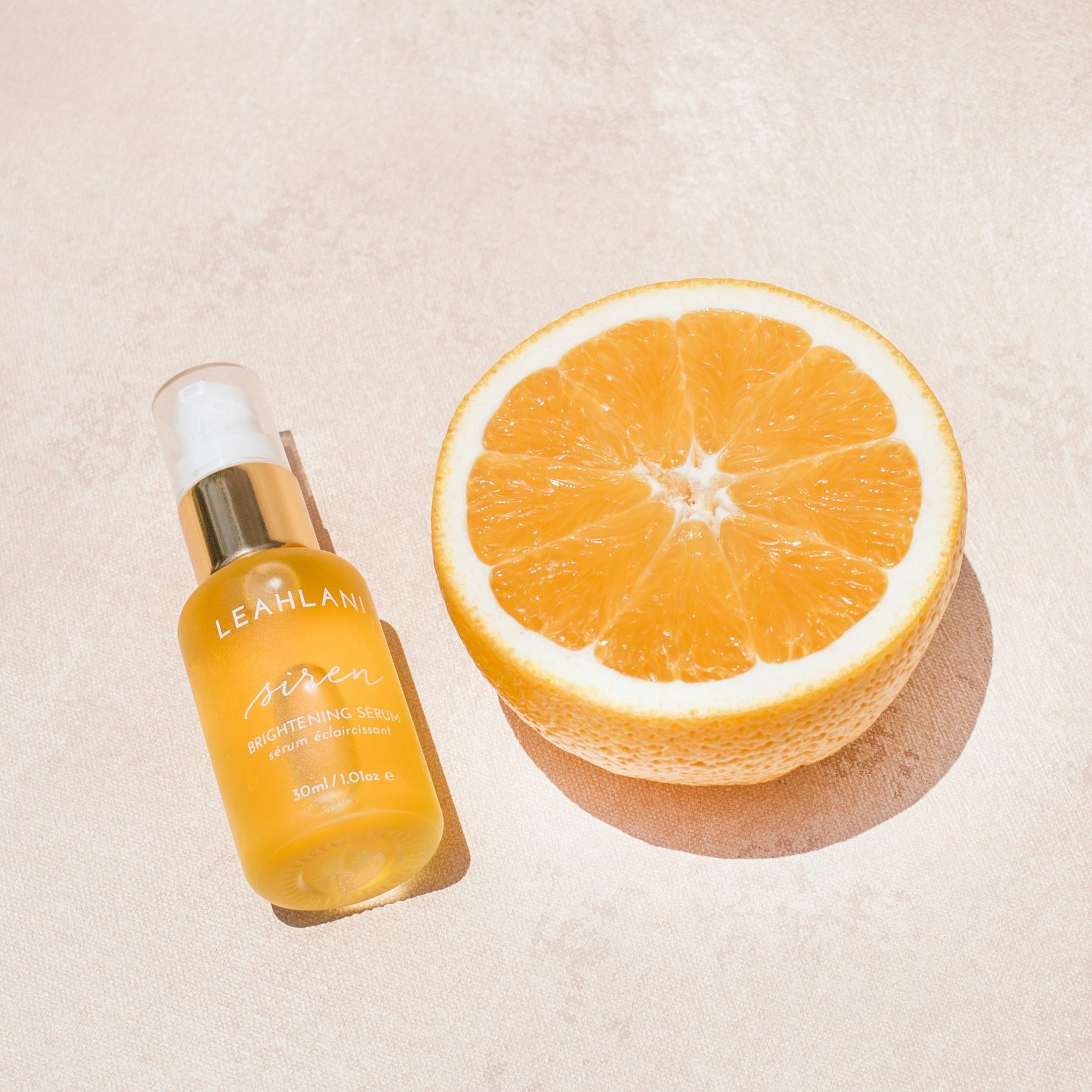 Leahlani Siren Serum Flasche liegend mit aufgeschnittener Orange auf hellem Hintergrund