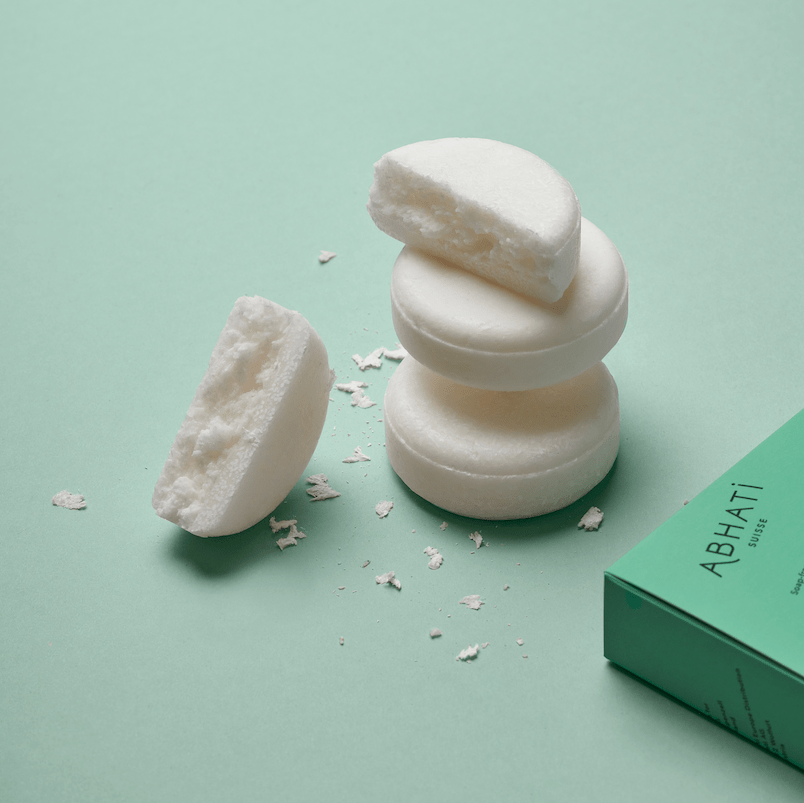 Aufeinandergestapelte Abhati Suisse Tanu Seifenstücke, eins in 2 Hälften gebrochen, liegen auf hellgrünem Untergrund.