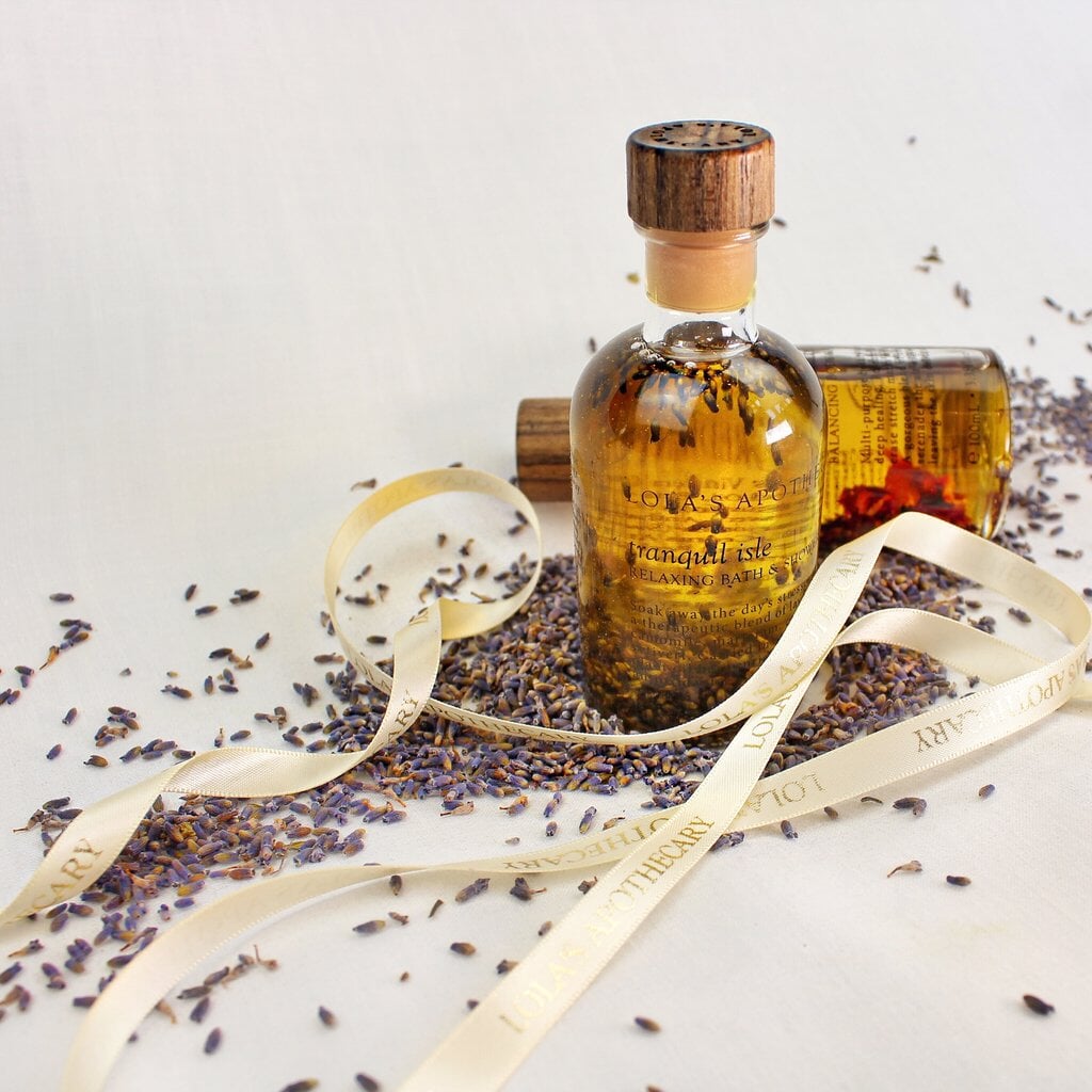 Mit Korken verschlossene Glasflasche Tranquil Isel Duschöl von Lola's Apothecary steht auf einem Bett aus Lavendelblüten.