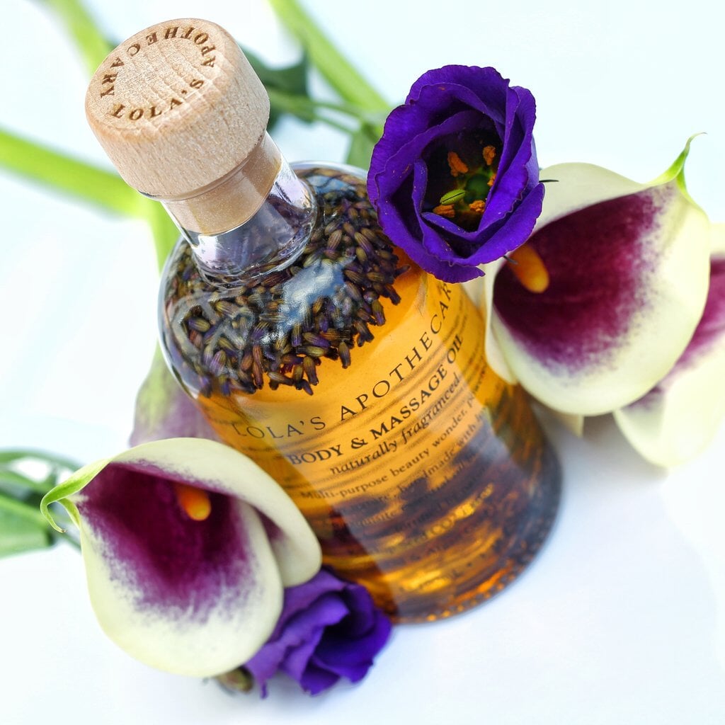 Glasflasche Body- und Massageöl von Lola´s Apothecary umgeben von Blüten.