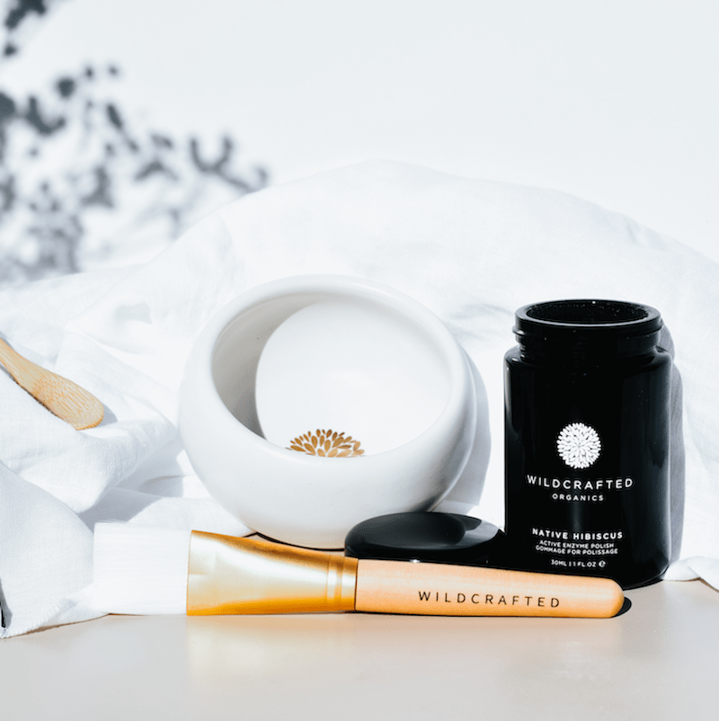 Wildcrafted Organics Vegan Masque Brush liegt vor einem weißem Schälchen und dem offenem Tiegel der Native Hibiscus Masque.