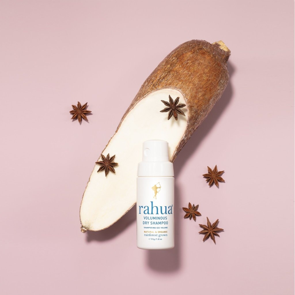 Rahua Voluminous Dry Shampoo Flasche vor rosafarbenem Hintergrund dekoriert mit Sternanis und aufgeschnittener Maniokwurzel. 