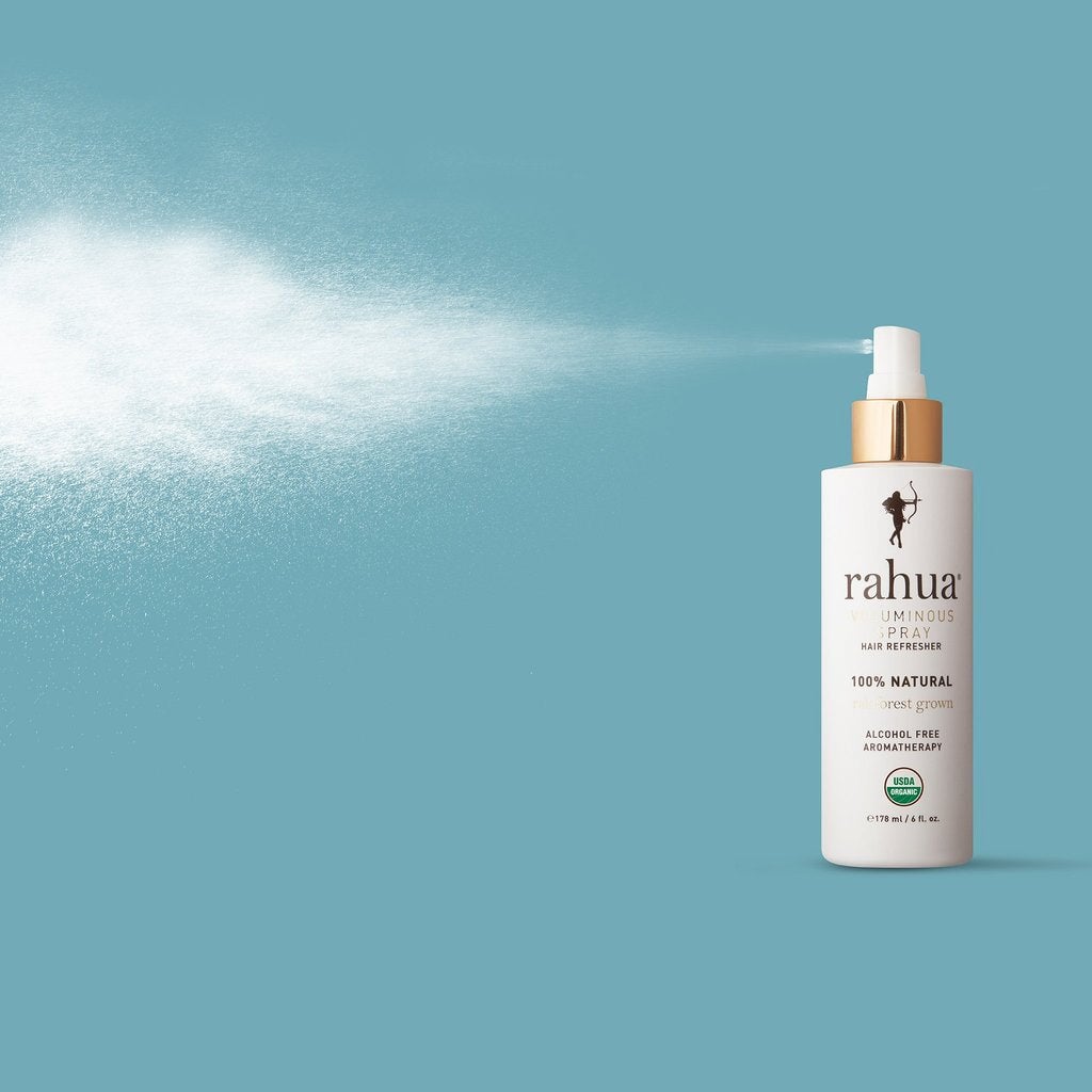 Rahua Voluminous Spray Flasche sprüht Haarspray vor blauem Hintergrund.