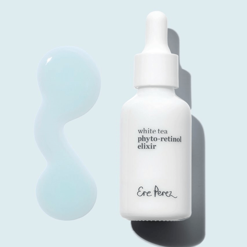 Weiße Flasche Ere Perez White Tea Phyto-Retinol Elixir liegt neben Texturbeispiel auf hellblauem Untergrund.