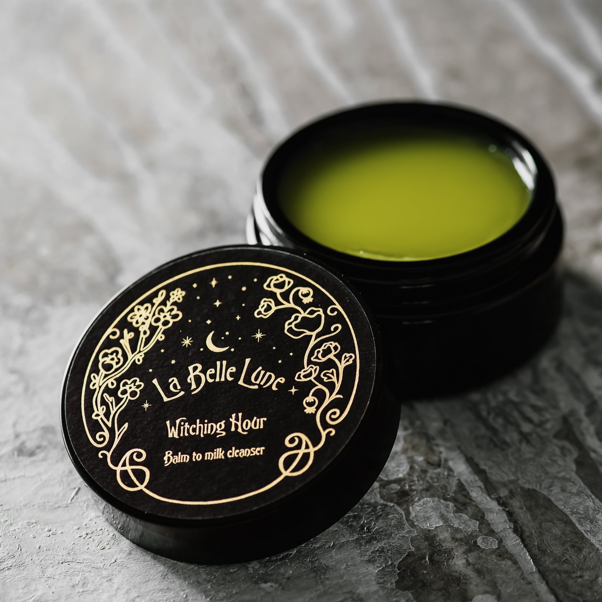 Cremige Textur des Witching Hour Cleansers – zart grünlicher Balm in geöffneter Glasverpackung

