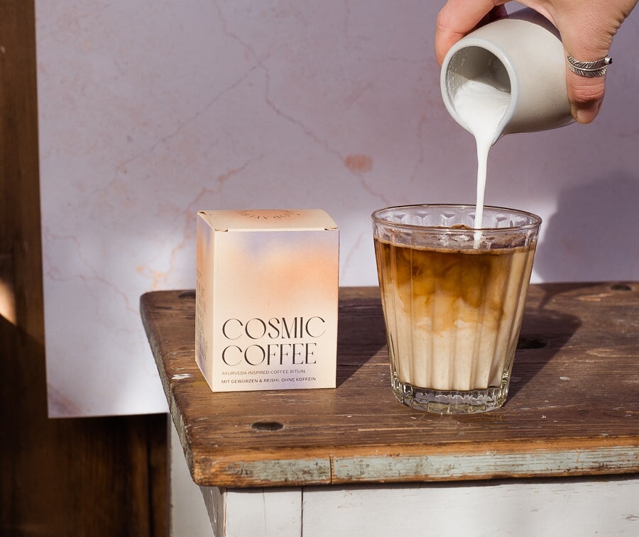 Cosmic Coffee packaging next to a glass in which the freshly prepared Ayurveda coffee is poured.
