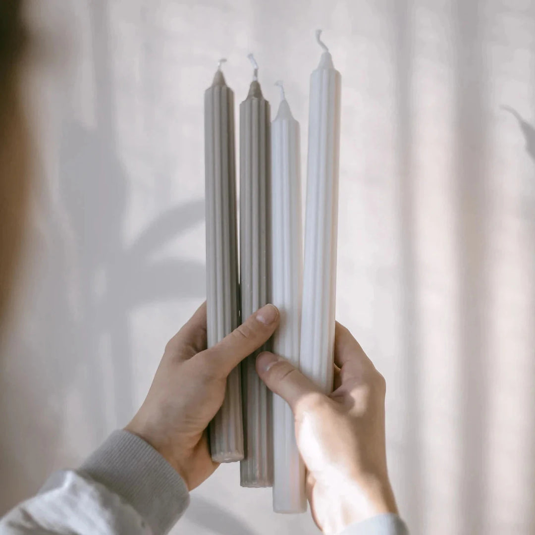 Two hands hold two white and two gray stick candles from Eulenschnnitt.