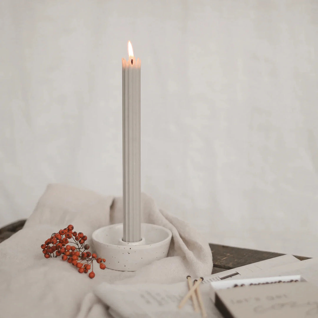 Lighted gray stick candle from Eulenschnitt in a candle holder on a beige linen cloth. North Glow