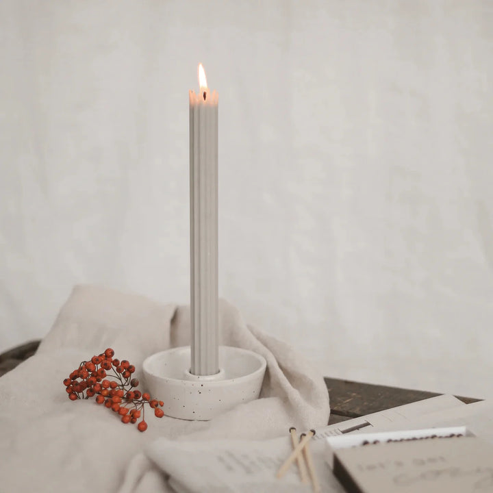 Lighted gray stick candle from Eulenschnitt in a candle holder on a beige linen cloth.