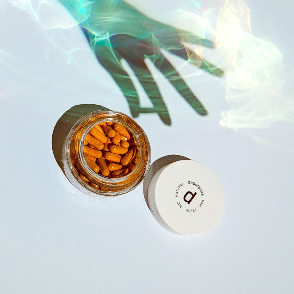 A shadowy hand reflected in the water reaches for an open screw-top jar of Depuravita Absolute Shine capsules.