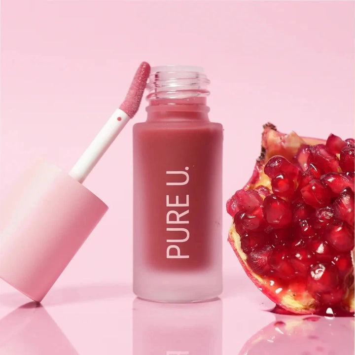 Balmy Lip Tint open, next to an open pomegranate against a pink background 