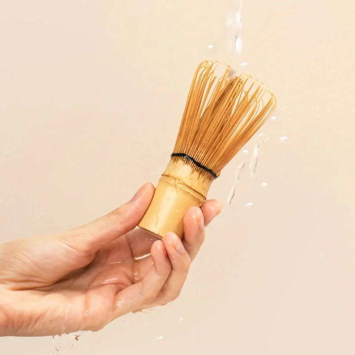 Hand hält Bamboo Whisk von MATCHA & CO unter fließend Wasser zum Ausspülen
