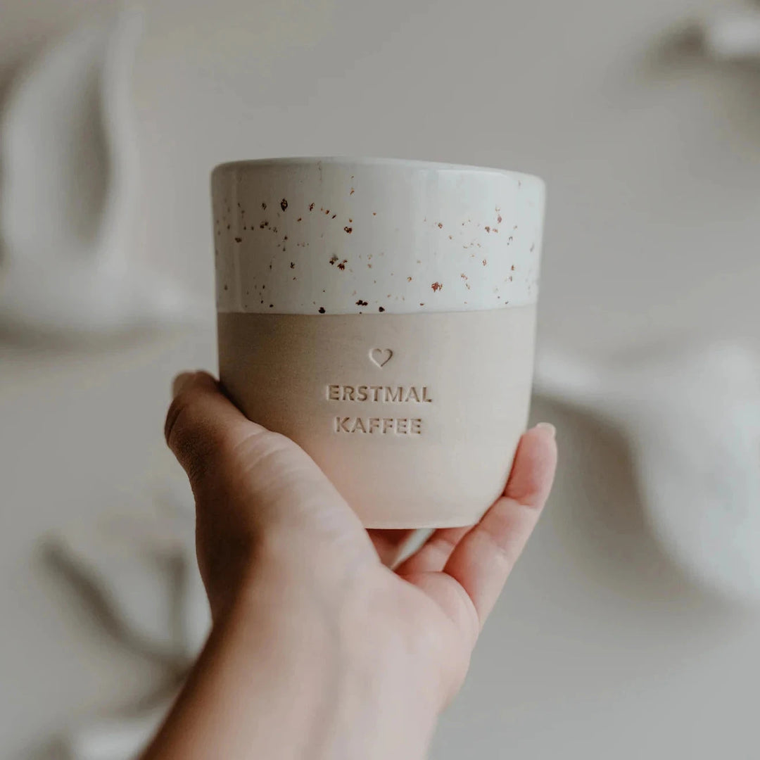 Coffee mug with embossing "Erstmal Kaffee" by Eulenschnitt is held in one hand.