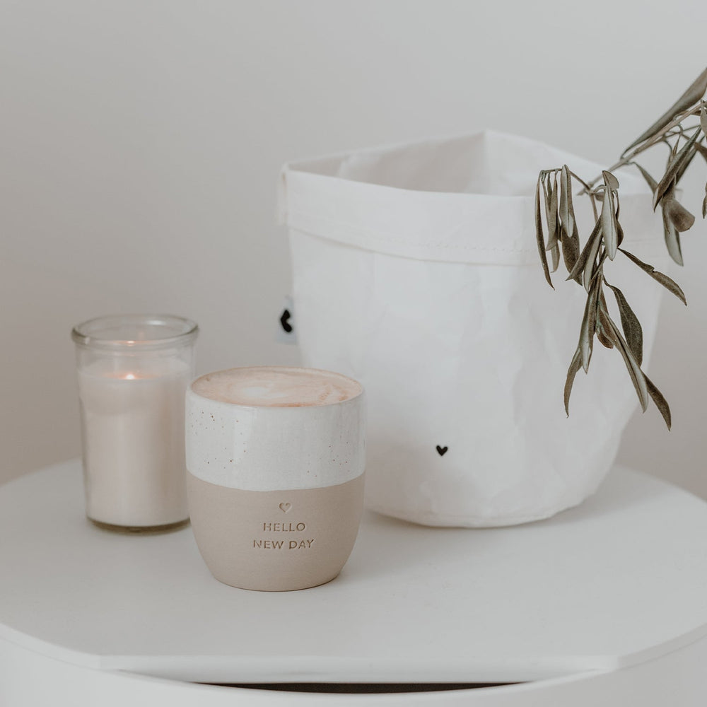 Hello New Day owl mug stands next to a burning candle and a white container with a heart.