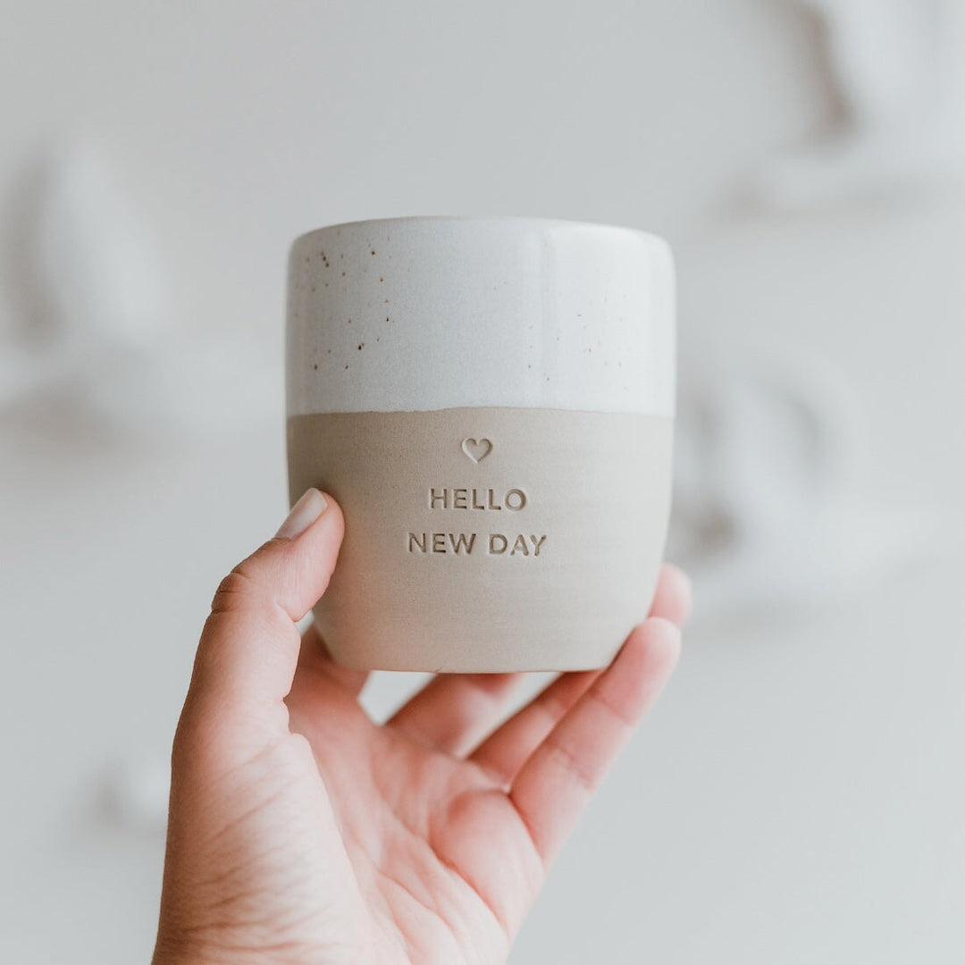 Hand holding owl cut mug Hello New Day in front of light background.