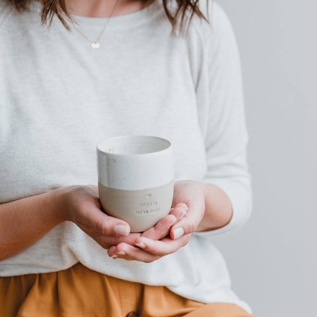 Woman in background, both hands holding owl cut mug Hello New Day. North Glow
