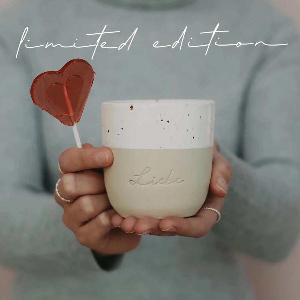 "Love" mug from Eulenschnitt is held by two hands together with a heart lollipop