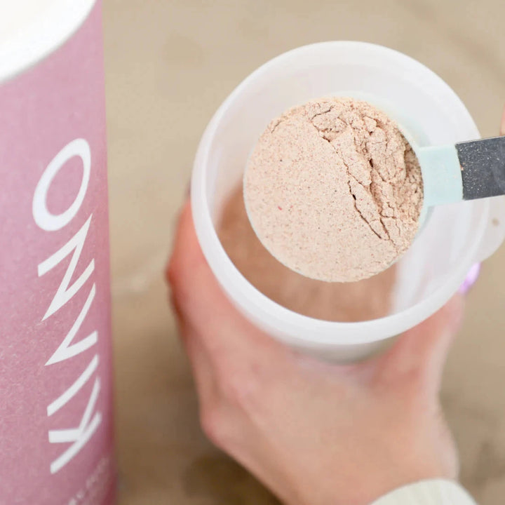 Hand holding container where spoonful of Kiano Berry Fuel powder is filled in 