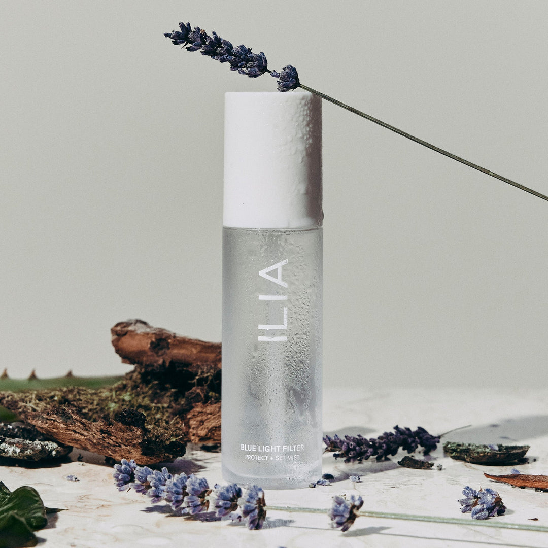 ILIA Blue Light Mist glass bottle with white lid is decorated with lavender on a light background.