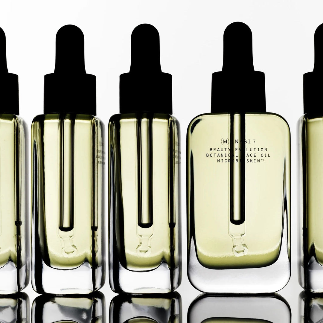Manasi 7 Botanical Faceoil Armonia bottles lined up stand on mirrored background.