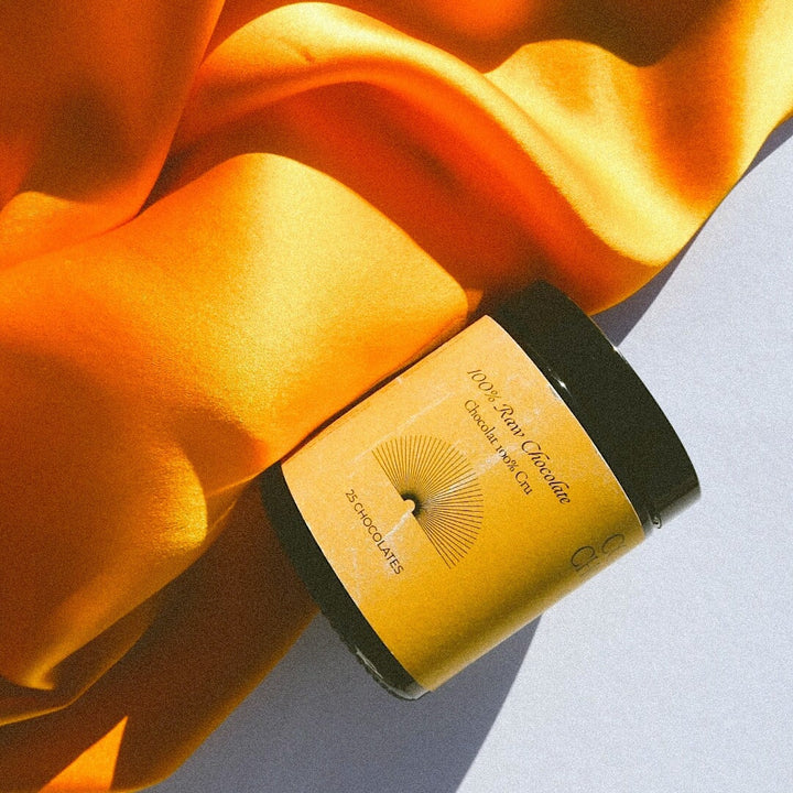 Depuravita Collagen Chocolates screw-top jar lies on an orange-colored blanket.