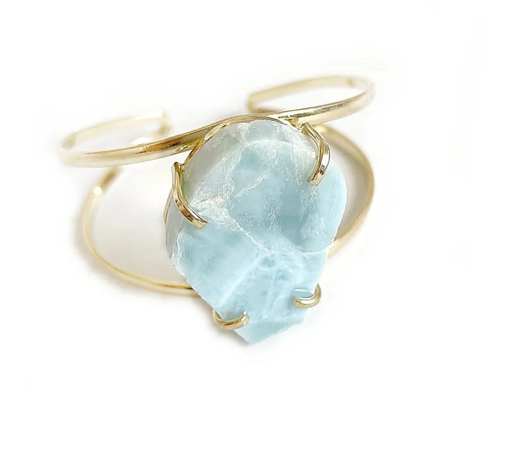 Gold-plated bangle with a turquoise-colored Larimar gemstone lying against a white background.