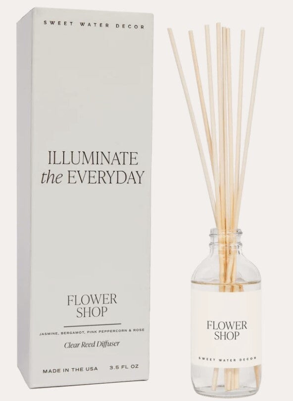 Transparente Flasche Raumduft Flower Shop Sweet Water Decor mit Schilfrohrstangen steht neben der Verpackung vor hellem Hintergrund. North Glow