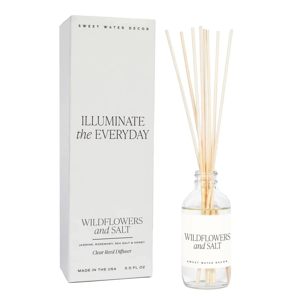 Transparente Flasche Diffuser Wildflowers and Salt von Sweet Water Decor mit Schilfrohrstangen, steht neben der Verpackung vor transparentem Hintergrund.