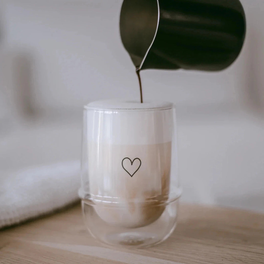 Double-walled latte machiato glass with heart by eulenschnitt is filled with coffee from a small jug.