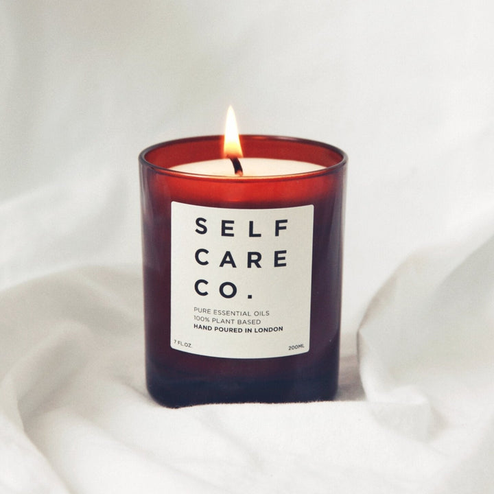 Brown candle jar with the inscription Self Care Co. stands on a white cloth