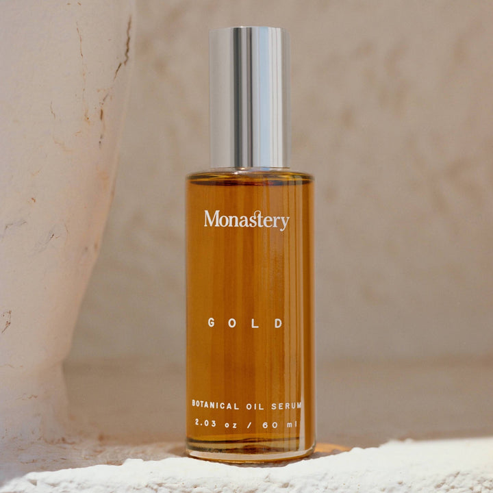 Monastery Gold Serum glass bottle with silver lid stands on a limestone rock.