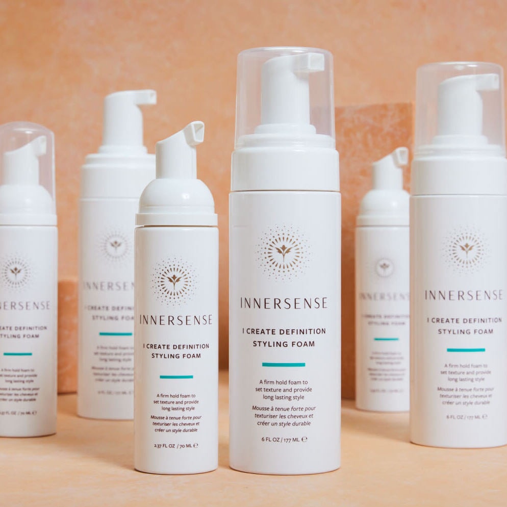 6 products from the Innersense I Create series stand on an apricot-colored surface. North Glow