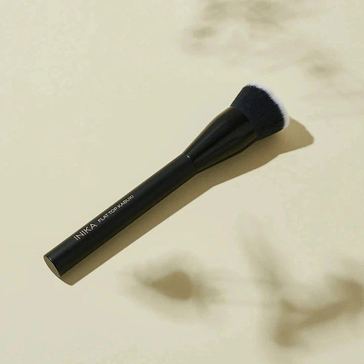 INIKA Flat Top Kabuki Brush black brush on beige background.