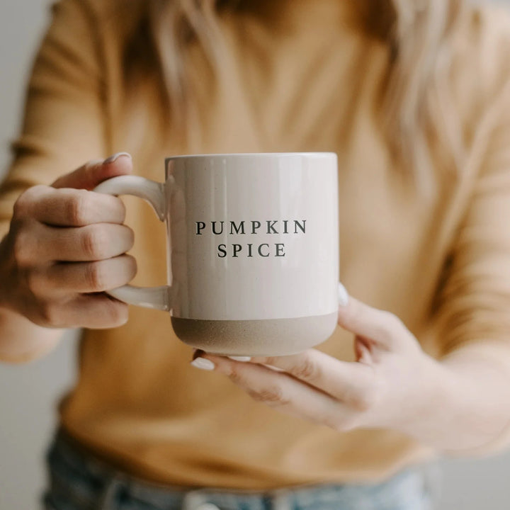 Cremefarbene Kaffeetasse Pumpkin Spice von Sweet Water Decor wird von 2 Händen einer blonden Frau in orangefarbenem Pullover gehalten.